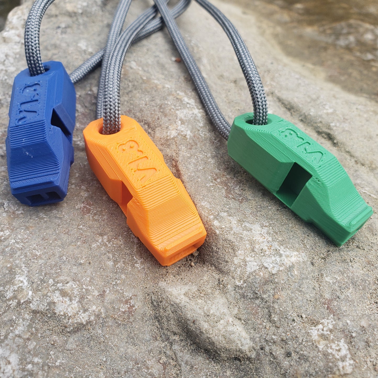 Three colorful whistles with straps on a stone surface