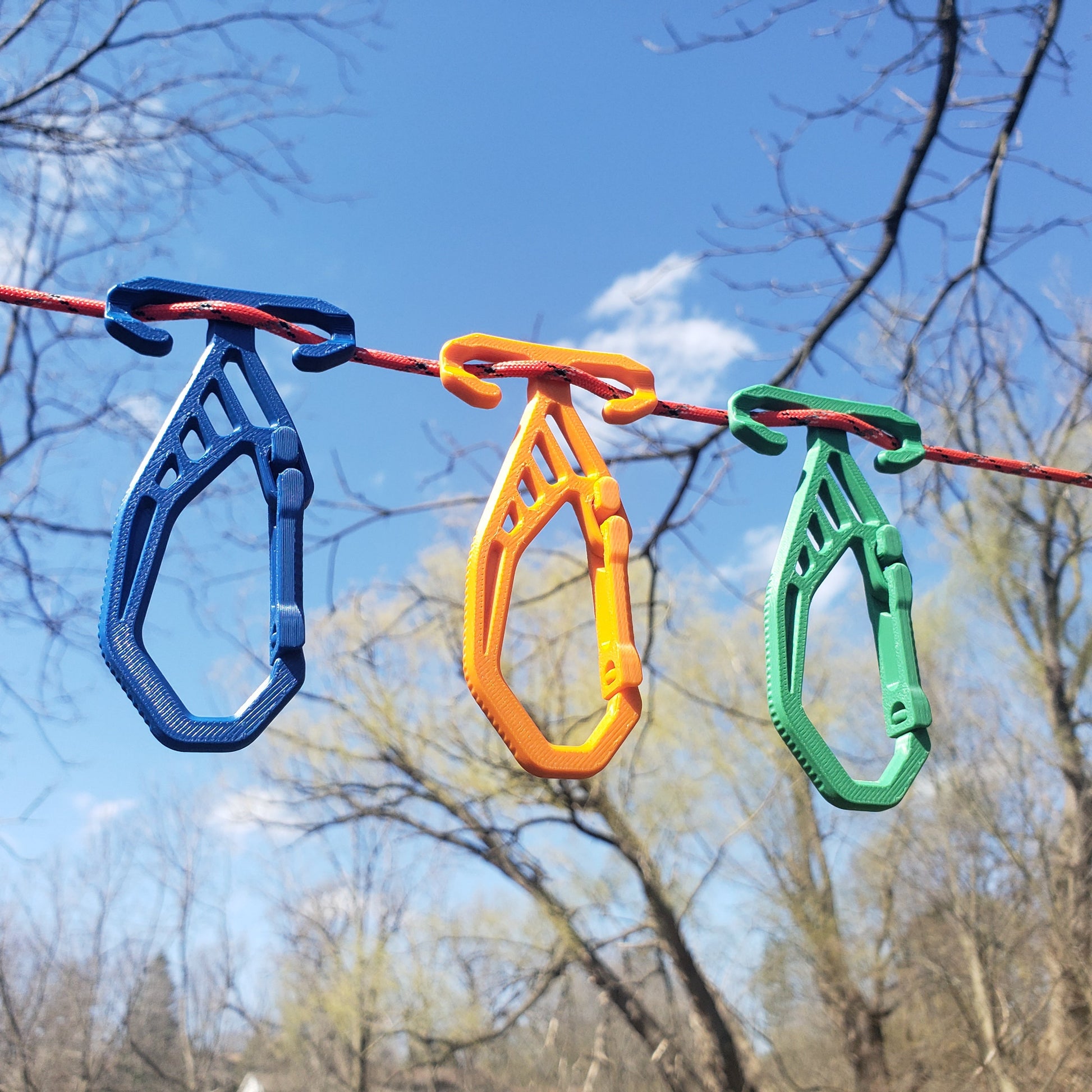 Three colorful RidgeClips on a rope with a blue sky and tree branches in the background
